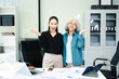 © Nuttapong punna - Confident Asian businesswomen standing in modern office. Leadership, teamwork, mentoring and corporate success concept with laptop and documents.