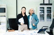 © Nuttapong punna - Confident Asian businesswomen standing in modern office. Leadership, teamwork, mentoring and corporate success concept with laptop and documents.