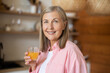 © zinkevych - Smiling woman standing at home holding a glass of orange juice