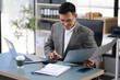 © NINENII - Man calculating finances at home office desk with calculator and papers.