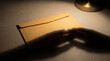 © MYKHAILO KUSHEI - A plain manila envelope sits on a desk. Shadowy hands reach for the sealed letter, illuminated by the warm light of a nearby lamp, hinting at anticipation or intrigue.