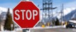 © pvl0707 - Handwritten stop sign on a rural road near a high-voltage pole and transformer against a clear blue sky, with mountains in the background