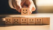 © Md - Hand selecting a wooden block with a happy smiley face over sad and neutral faces for customer experience choice