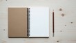 © AK_KADER - Minimalist top down view of an open spiral bound notebook with one blank white page and one blank kraft paper page resting beside a sharpened pencil on light wood surface