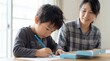 © Meow Creations - Focused asian boy drawing with blue pencil on paper while smiling mother watches him at home table