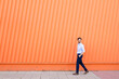 © VISTA by Westend61 - Business man walking by orange wall outdoors with copy space
