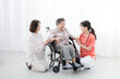 © kapinon - 病院や訪問介護で車椅子の高齢者の患者と家族を看護師が支える全身　在宅やショートステイなど医療の会話するイメージ