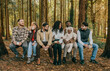 © Reuben - A group of people are sitting on a log in a forest. They are all smiling and enjoying each other's company