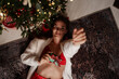 © svetograph - Christmas woman gift attractive lady lying under decorated tree enjoying cozy holiday mood