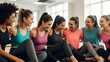© mumtaz - Group of diverse women in athletic wear sitting together in a gym or fitness studio smiling and enjoying a friendly workout session or fitness class