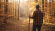 © Vasiliy - Rear view of a male hiker standing in an autumn forest holding a walking stick. Man in plaid shirt looking at golden sunlight in the woods. Fall season outdoor adventure concept