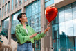 © Iryna - Woman holds red heart balloon outside modern building in urban area during daytime