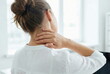 © CK Studio - Woman suffering from neck pain and shoulder tension while working in a bright office, massaging her painful neck for relief.