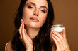 © Beauty Hero - Gentle young woman in beige background showcasing skincare cream with flawless makeup and glowing skin