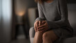 © INSPIRIA.K - Woman sitting on sofa and holding her painful knee joint at home