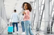 © Prostock-studio - Travel Concept. Portrait of smiling excited African American teenage girl walking with suitcase at airport terminal corridor, showing thumbs up sign gesture, looking back at camera, enjoying vacation