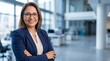 © Николай Срибяник - Portrait of a confident middle aged Hispanic businesswoman smiling with arms crossed in a modern corporate office wearing glasses and a blue blazer