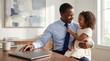 © Николай Срибяник - Smiling Black executive father sitting at desk with daughter on lap pulling his tie during work break in bright home office