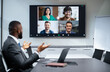 © Prostock-studio - A group of four people joins a video call while one participant talks from a conference room. The setting showcases a modern workspace with laptops and a large screen displaying faces.