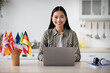 © Prostock-studio - Pretty asian lady student looking for online school, sitting at kitchen with laptop, copy space. Cheerful young woman seeking foreign languages course on Internet, home interior. E-education concept