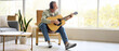 © Pixel-Shot - Mature man in headphones playing guitar at home