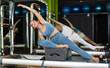 © JackF - Woman in sports top and leggings doing bends while sitting on a reformer. Pilates workout visitor doing exercises for abdominal muscles