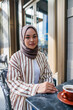 © Jovo Jovanovic/Stocksy - Woman in hijab enjoys coffee at an outdoor cafe.
