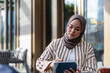 © Jovo Jovanovic/Stocksy - Woman in hijab uses tablet at outdoor cafe.