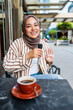 © Jovo Jovanovic/Stocksy - Smiling woman in hijab speaks into microphone with coffee.