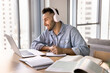 © fizkes - Young 30s Hispanic man listen to audio class using modern wireless headphones, taking notes in notebook, engaged in online course, participate in webinar for gaining new knowledge remotely. E-learning
