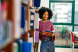 © Wanwajee - Young Black student stands beside library shelves, holding book and smile to camera. Show confidence curiosity literacy development independent learning diversity supportive education environment.
