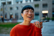 © Artcore Studio/Stocksy - Asian woman sending voice message with smartphone outdoors