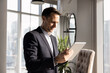 © fizkes - Positive young Hispanic executive man typing on tablet, standing in office, holding gadget, using online technology, financial application for managing business process, enjoying communication