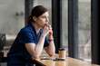 © NAMPIX - Tired female doctor or nurse with stethoscope looking out window, thinking in cafe.
