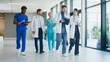 © VAKSMANV - Medical staff walking calmly along bright corridor inside modern hospital. Focused doctors reviewing notes while discussing plans. Nurses joining conversation and moving together during routine moment