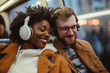 © MarsPacific - Two smiling passengers, a woman with curly hair and a man with glasses, wearing headphones and sitting close together on a bus or train.