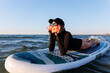 © Kyryl Gorlov - Smiling woman enjoys surfing on Baltic Sea waves, laughing joyfully lying on board with splashing water around. Bright sunlight and her laughter reflect pure joy, freedom and vibrant summer adventure
