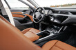 © ARTUR - Premium, modern brown interior of an electric car, leather steering wheel, large navigation screen, air ducts, deflectors on the car panel. Interior details.