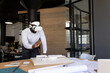 © Wavebreak Media - African American man wearing white VR headset, leaning over model and blueprints at office table