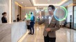 © DesignSells - Business professional interacting with a holographic interface displaying charts and circular graphics in a modern lobby reception area.