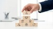 © Gayan - Close up of a professional Southeast Asian businessman in a dark suit stacking wooden blocks with icons for customer loyalty, satisfaction, and rewards in a bright high-key office environment.