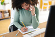 © Studio Marmellata - A woman with curly hair talks on her phone while writing in a notebook at her desk.