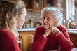 © EricMiguel - Warm intergenerational moment: smiling senior woman in cozy red sweater sharing a heartfelt conversation with younger family member in a kitchen