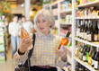 © JackF - Mature woman chooses Italian wine in the alcohol department of a hypermarket. Adult woman with gray hair choosing semi-sweet wine for dinner