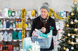 © JackF - Elderly man in winter clothes makes purchases of household chemicals for New Year's promotions and sales. Pensioner with a full basket of goods in a household supermarket against the background of a