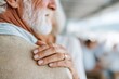 © TesaI - Woman's hand with wedding ring resting on senior man's shoulder, symbolizing lasting love, support, comfort, and devotion