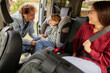 © Stockphotodirectors - Parents assist their young child in fastening the car seat in a vehicle, showcasing a moment of love and care before embarking on a fun outing together.