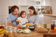 © Stockphotodirectors - In a warm kitchen, a family gathers around a table, happily preparing snacks. The child stirs a bowl while parents assist, sharing moments of laughter and joy.