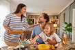 © Stockphotodirectors - A mother and father share a light moment at the breakfast table while their curious child explores food options. Warm sunlight fills the inviting room, creating a cheerful scene.