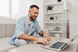 © SHOTPRIME STUDIO - Smiling man working on laptop from home, reflecting modern remote work culture and embracing technology in a cozy environment. Focus on productivity and comfort.